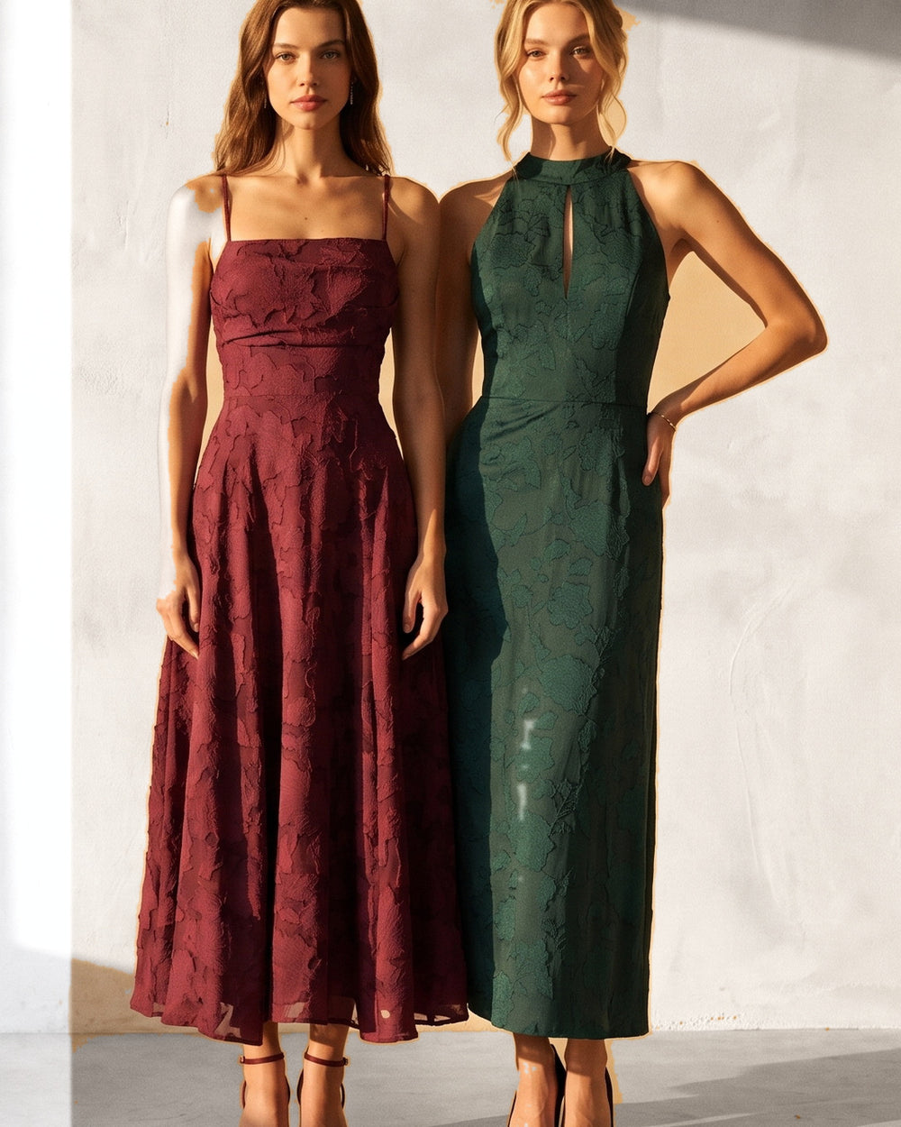 Two models in wine and emerald jacquard maxi dresses in a sunlit ivory room