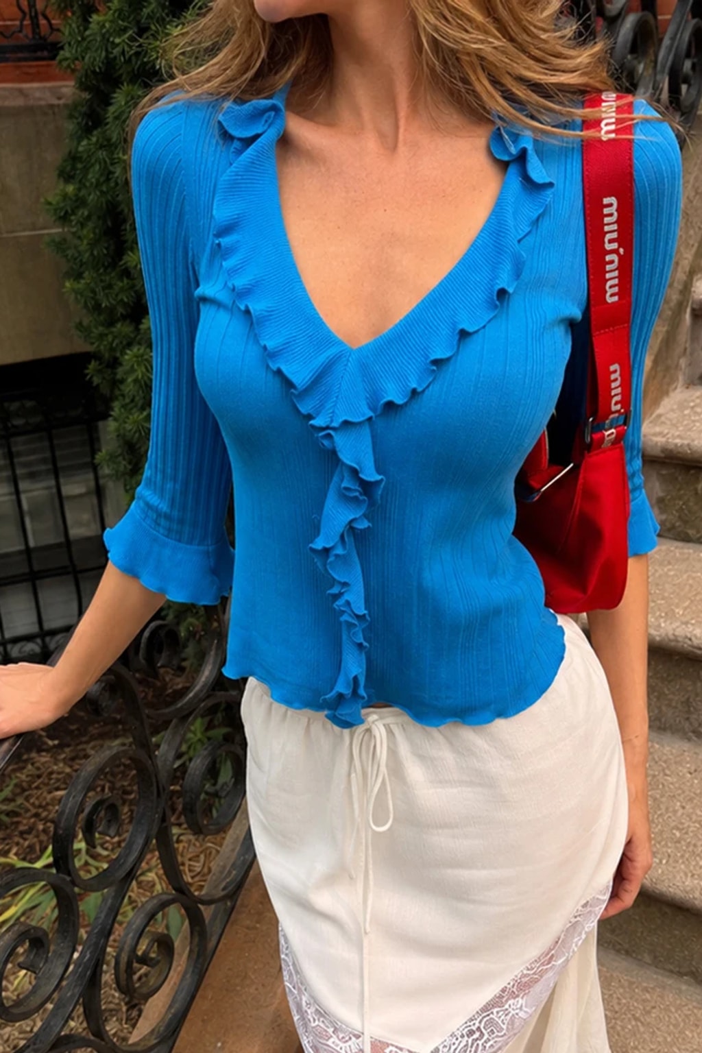 Ribbed knit pullover top with a ruffle trim down the front V neckline and three-quarter flared sleeves with tie cuffs