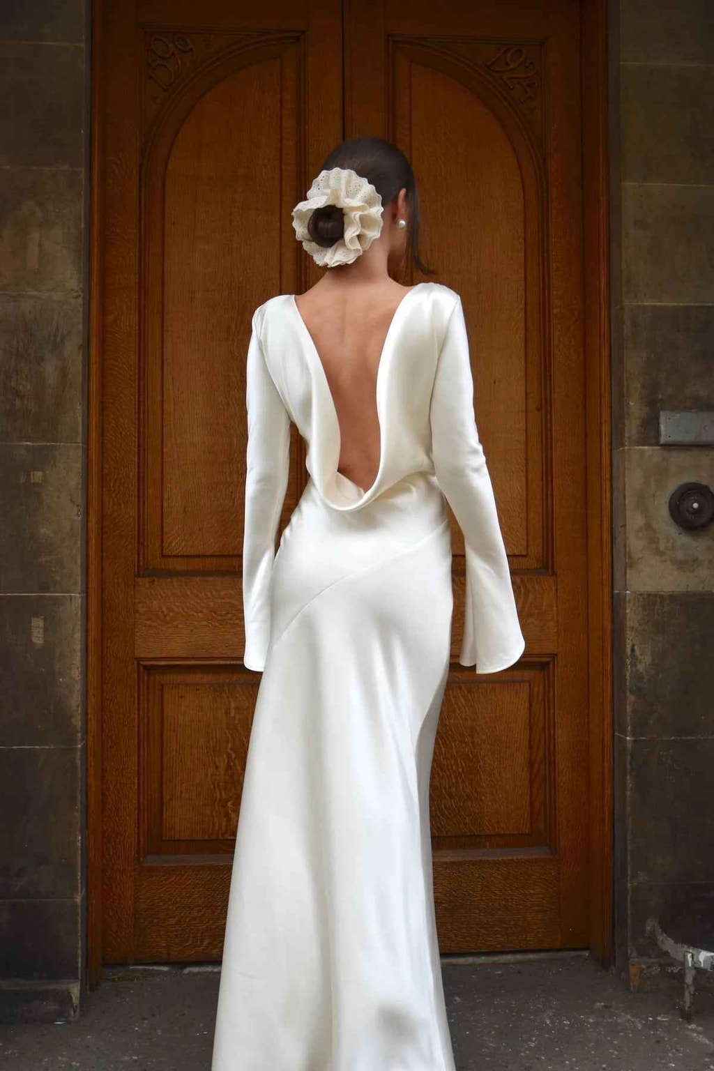 Model wearing the ivory satin gown at a carved wooden door, showing the deep scooped cowl open back
