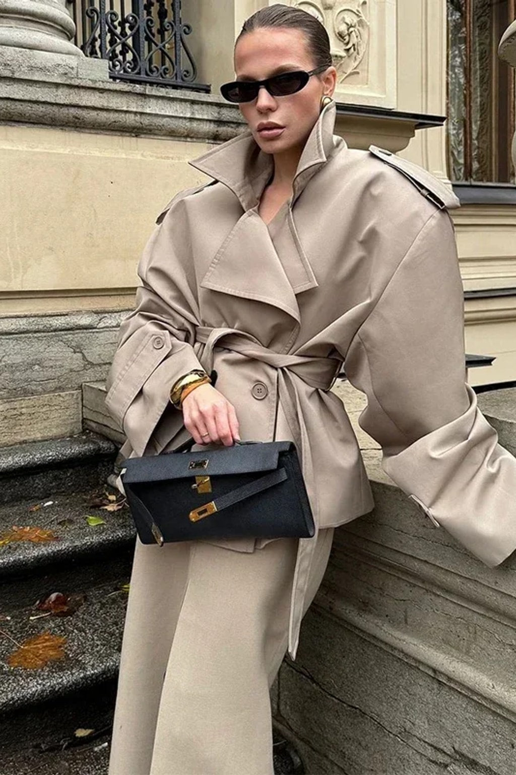 Beige cropped trench jacket that wraps across the front with a self-tie belt, epaulettes and buttoned cuff tabs